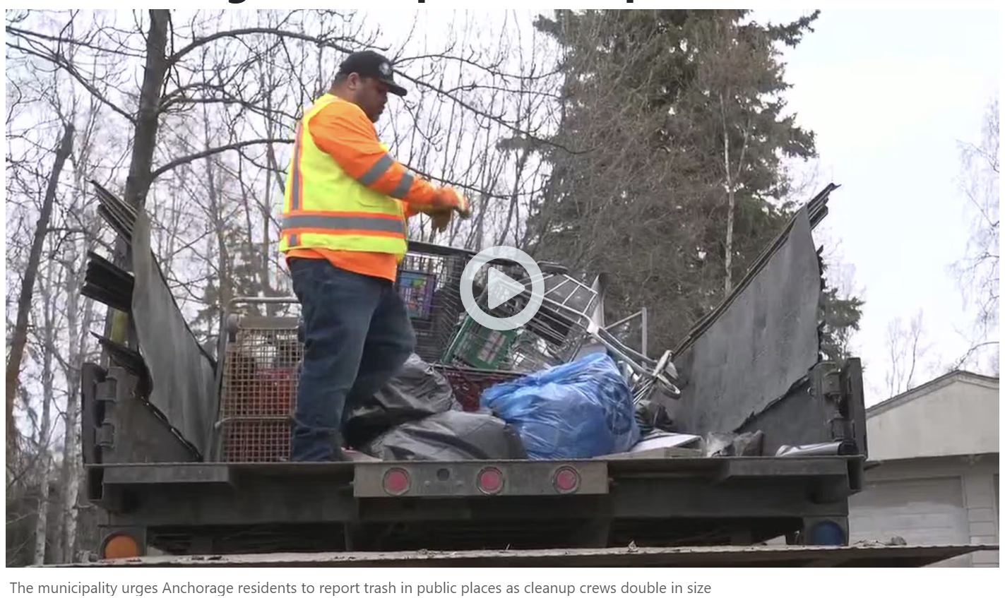 Sanitation worker in an orange safety jacket on a dump truck filled with trash and discarded items during a cleanup effort