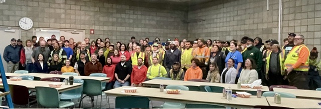MOA Safety Meeting 2026-5-14 - LIUNA Public Employees Local 71 Large group of coworkers in a workplace cafeteria posing for a group photo, many wearing colorful safety vests and casual clothing.
