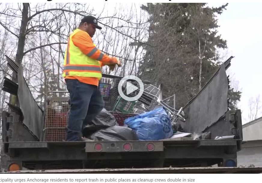 Sanitation worker in an orange safety jacket on a dump truck filled with trash and discarded items during a cleanup effort